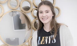 ein Mädchen steht mit Zahnspange vor goldenem Spiegel in der Praxis